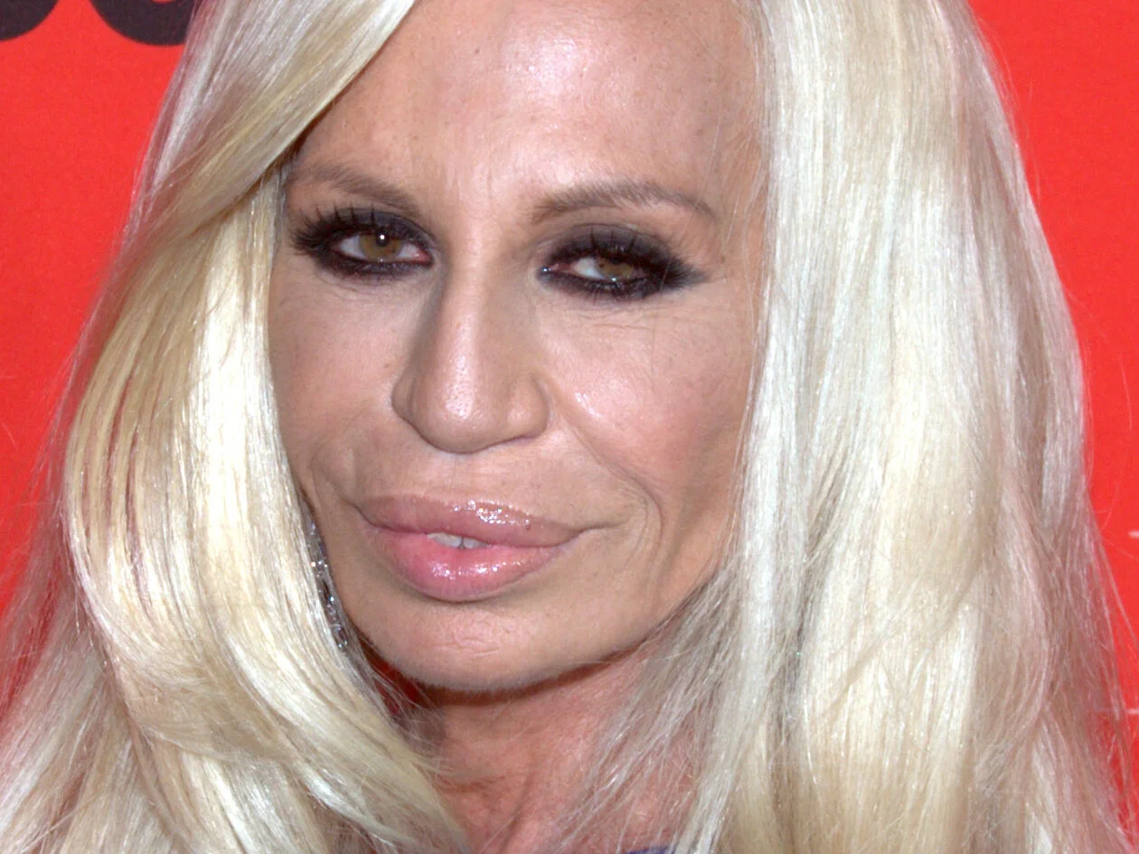 Närbild av Donatella Versace med långt platinablont hår framför en röd fotovägg 2010