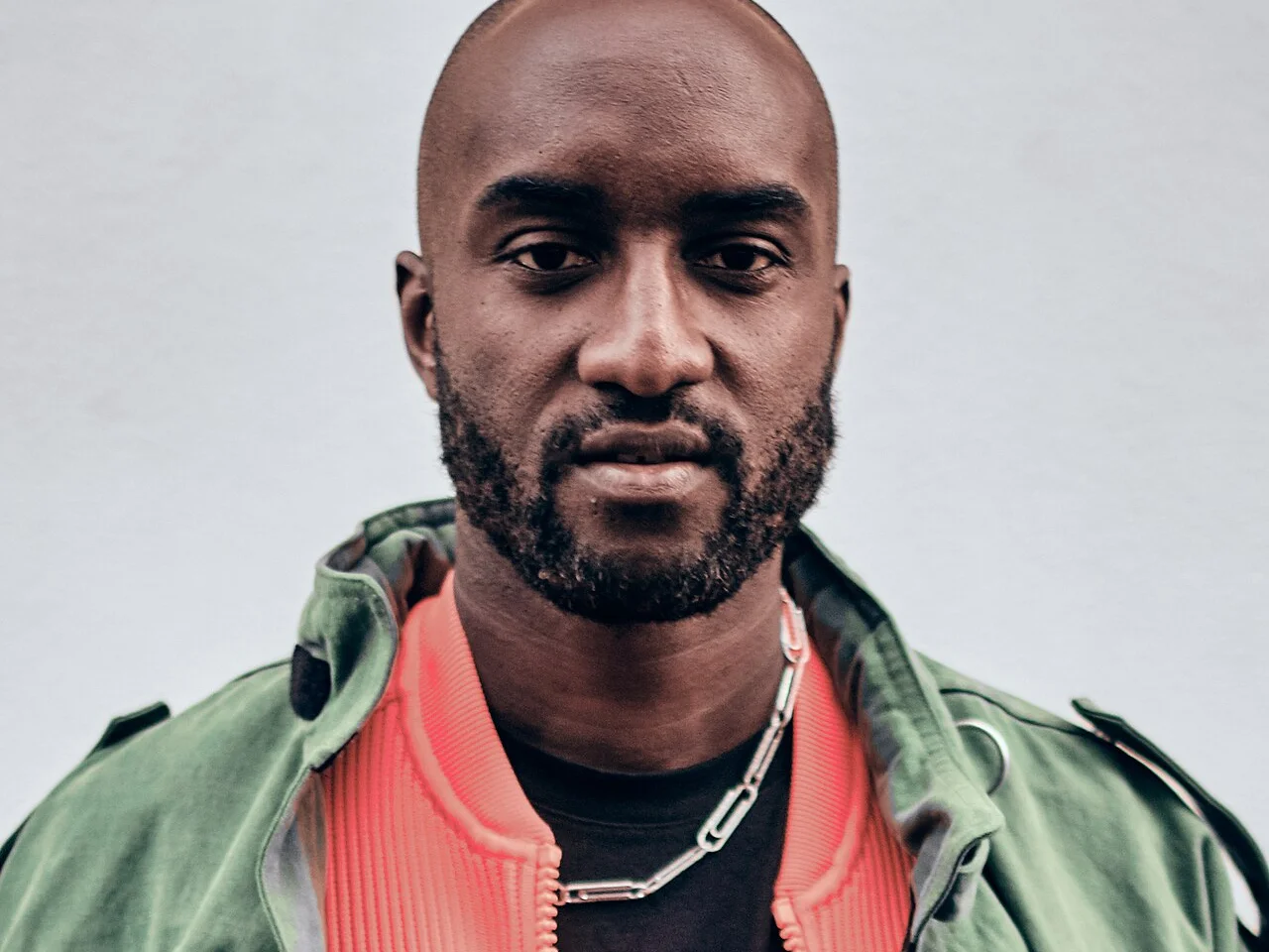 Porträtt av Virgil Abloh i grön jacka och korallröd collegejacka under Paris Fashion Week 2019